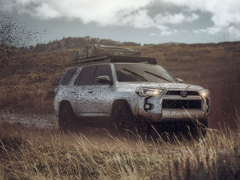 Load image into Gallery viewer, Toyota 4Runner equipped with Front Runner Slimline II Roof Rack driving on rough terrain showing durability and storage capability.