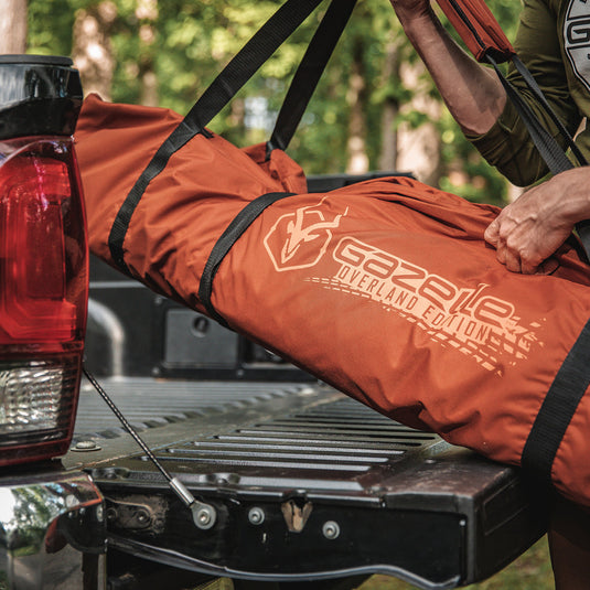 Person loading a Gazelle T4 Overland Edition water-resistant duffle bag onto a vehicle tailgate outdoors