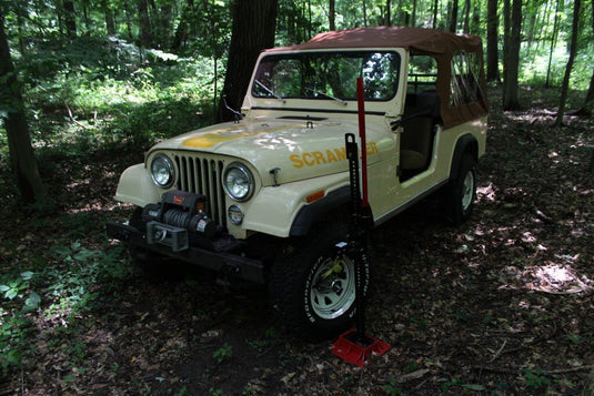 Red Hi-Lift Jack 60 Cast/Steel being used to lift a yellow off-road vehicle in a forested area.
