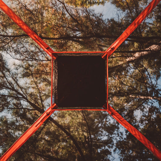 Looking up from inside a Gazelle T4 Hub Tent towards the trees, showcasing the sturdy red framework and spacious interior design.