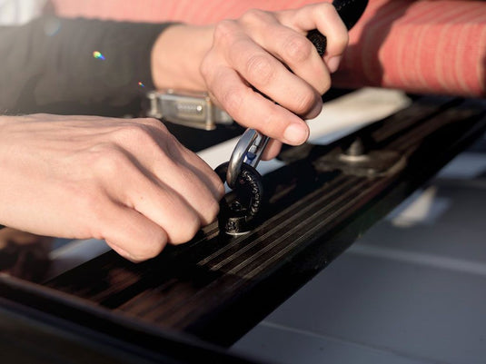 Hands securing equipment with Front Runner Black Tie Down Ring on vehicle roof rack