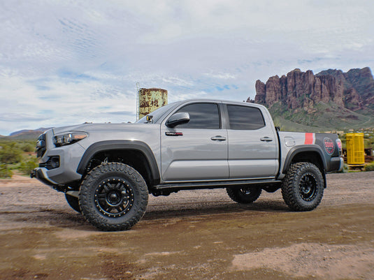 Silver pickup truck equipped with ICON Vehicle Dynamics Six Speed satin black wheels on off-road terrain.