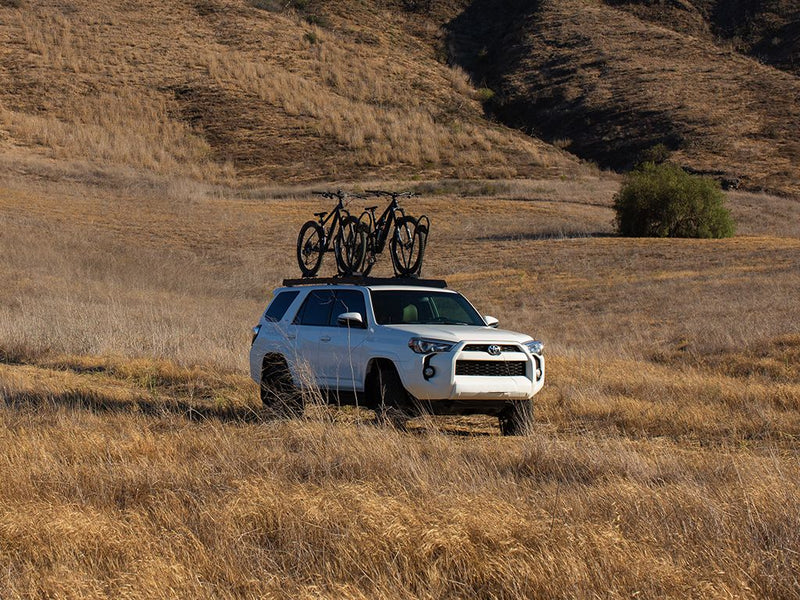 Load image into Gallery viewer, White Toyota 4Runner with Front Runner Slimsport Roof Rack Kit carrying bicycles, parked in grassy field.
