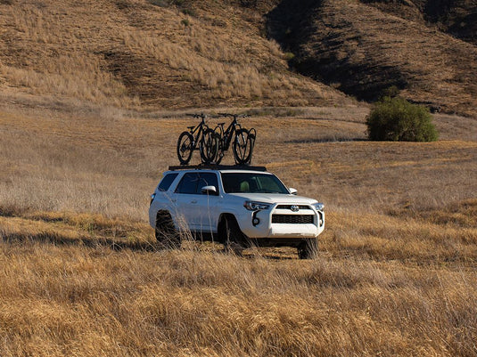 White Toyota 4Runner with Front Runner Slimsport Roof Rack Kit carrying bicycles, parked in grassy field.