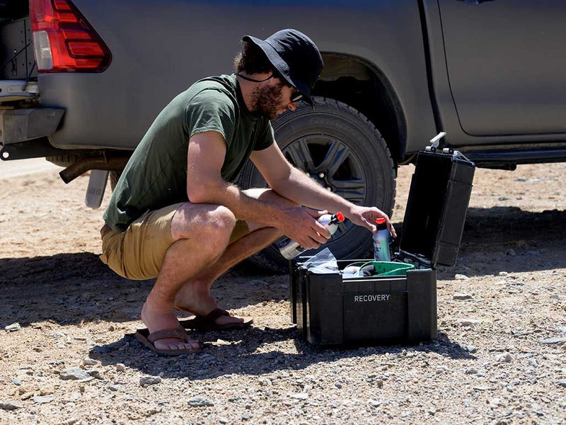 Load image into Gallery viewer, Man crouching by vehicle unpacking Front Runner Wolf Pack Pro Hi-Lid storage box during outdoor recovery activities.
