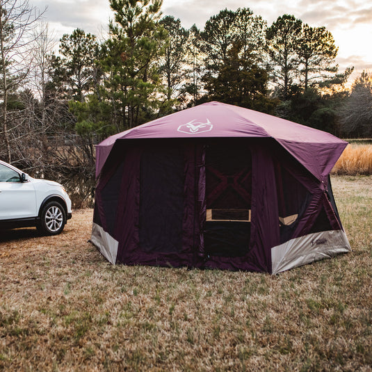 Alt text: "Gazelle Tents T-Hex Hub Tent Overland Edition set up in a field with trees in the background at dusk, showcasing spacious design and easy vehicle access for camping."