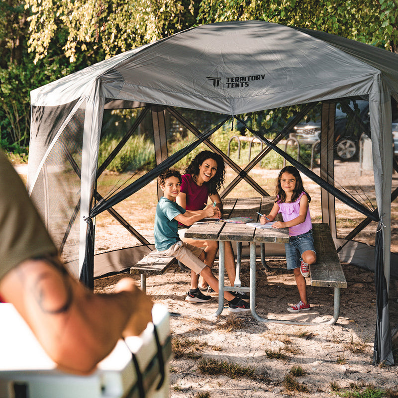 Load image into Gallery viewer, Family enjoying a picnic under the Territory Tents 6-Sided Screen Tent at a campsite.
