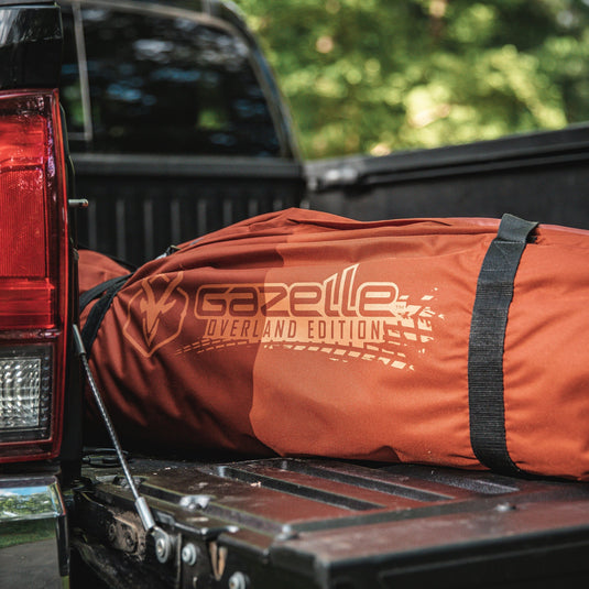 Gazelle Tents T4 Hub Tent Overland Edition packed in a branded orange carry bag, placed in the bed of a pickup truck ready for adventure.