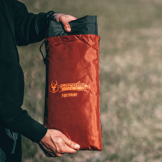 Alt text: "Person holding a folded Gazelle Tents T4 Tent Footprint in a red storage bag with the brand logo clearly visible."