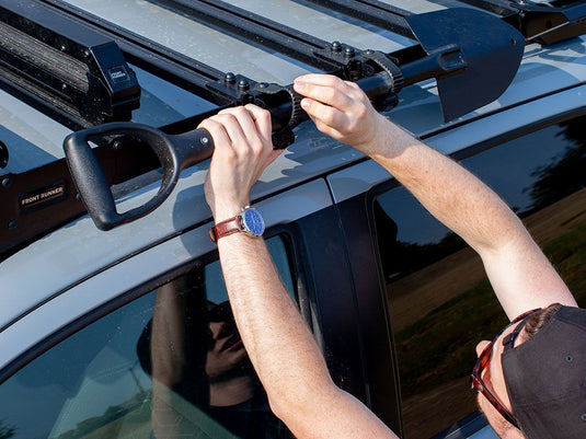 Person installing a Front Runner Slimsport Side Mount Accessory Bracket on a vehicle roof rack