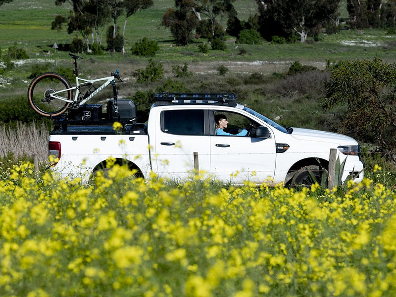 Load image into Gallery viewer, White pickup truck with Front Runner Load Bed Rack Side Mount and bike carrier on rear bed in nature.
