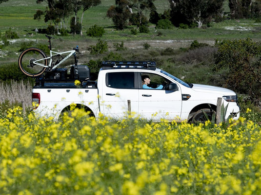 White pickup truck with Front Runner Load Bed Rack Side Mount and bike carrier on rear bed in nature.