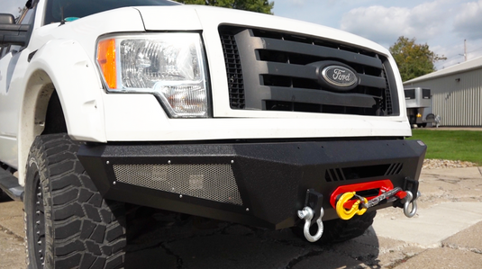 Alt text: "Fishbone Offroad 2009-2014 F-150 Pelican Front Bumper installed on Ford truck, featuring integrated winch mount and recovery points."