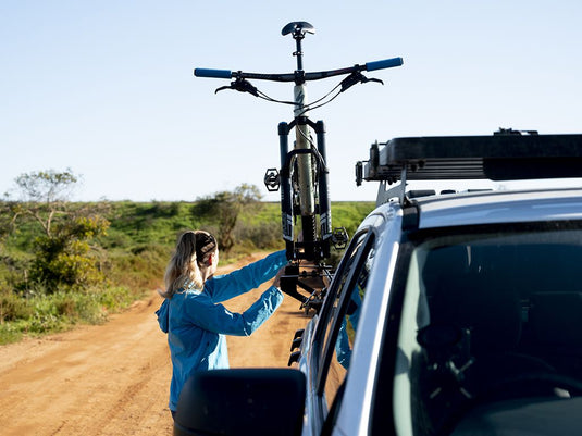 Woman attaching bike to Front Runner Load Bed Rack Side Mount on off-road vehicle