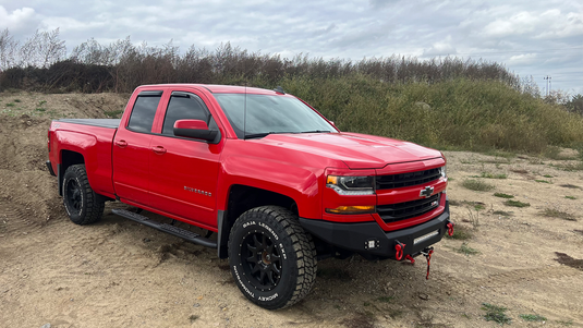 Alt text: "Red 2014-2019 Chevrolet Silverado Double Cab pickup with Fishbone Offroad 5-inch oval side steps installed, parked off-road."