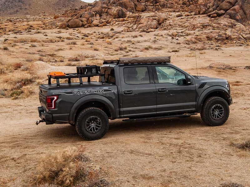 Load image into Gallery viewer, Ford F150 Raptor equipped with Front Runner Slimline II Load Bed Rack Kit parked in rugged terrain, showcasing the roll top 6.5-foot cargo management system for the 2015-current model.
