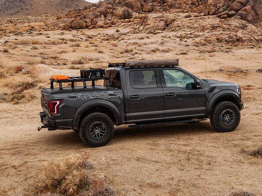 Ford F150 Raptor equipped with Front Runner Slimline II Load Bed Rack Kit parked in rugged terrain, showcasing the roll top 6.5-foot cargo management system for the 2015-current model.