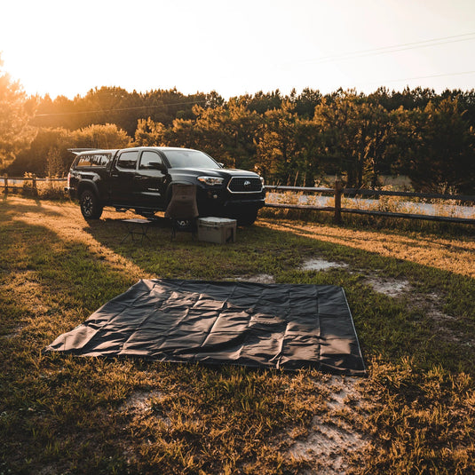 Gazelle Tents T4 Hub Tent Overland Edition laid out on ground next to a pickup truck in a camping setting during sunset.