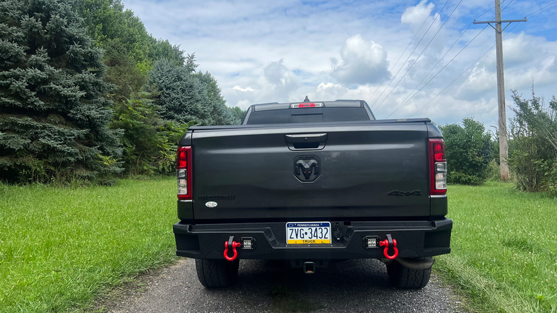 Load image into Gallery viewer, 2019-2023 Ram 1500 with Fishbone Offroad Pike Rear Bumper, featuring red tow hooks and black finish, parked outdoors.
