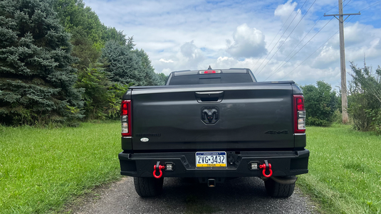 2019-2023 Ram 1500 with Fishbone Offroad Pike Rear Bumper, featuring red tow hooks and black finish, parked outdoors.