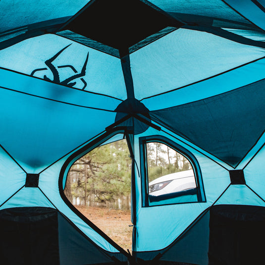 Inside view of Gazelle Tents T3X Overland Edition Tent with open window facing forest and car outside.