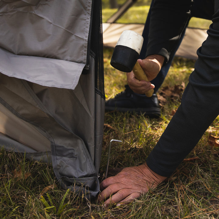 Load image into Gallery viewer, Person setting up a Territory Tents 4-Sided Portable Screen Tent outdoors using a rubber mallet to secure a peg.
