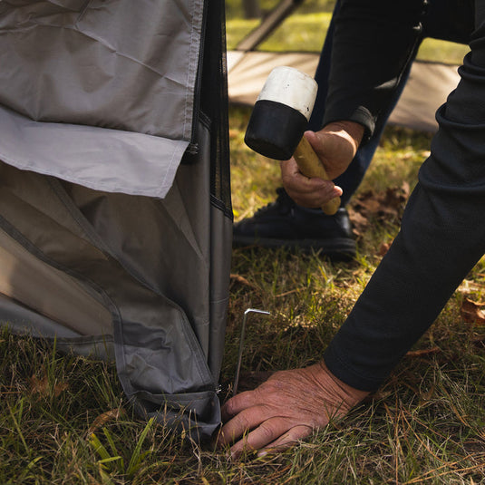 Person setting up a Territory Tents 4-Sided Portable Screen Tent outdoors using a rubber mallet to secure a peg.