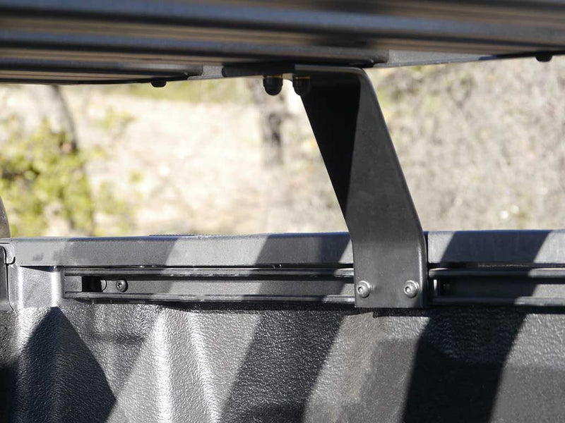 Load image into Gallery viewer, Close-up of the Front Runner Slimline II Load Bed Rack Kit installed on a Nissan Titan Pickup Truck model 2003-present, highlighting the durable mounting bracket system.
