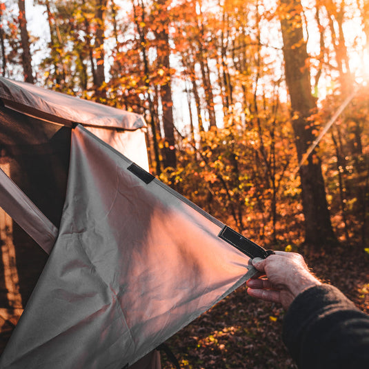 Alt text: "Person attaching a wind panel to a Gazelle Tents gazebo in a forest setting during sunset."
