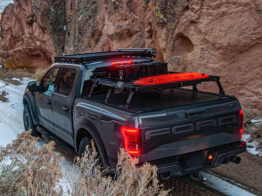 Ford F150 Raptor equipped with Front Runner Slimline II Load Bed Rack Kit and Roll Top, parked outdoors with rock formations in the background.