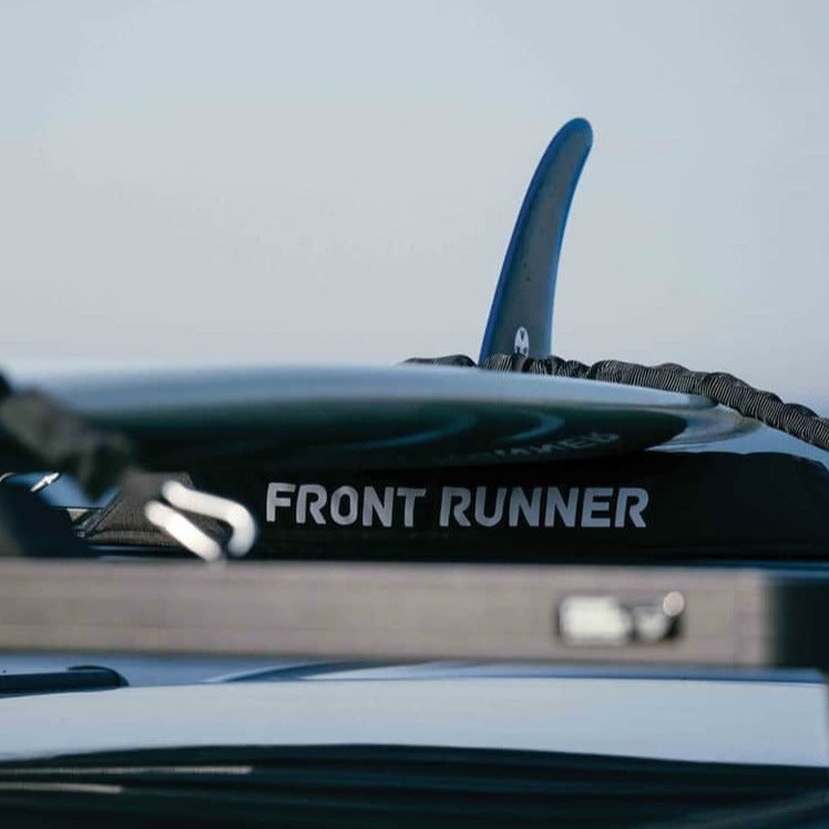 Load image into Gallery viewer, Close-up of Front Runner Rack Pad Set mounted on a vehicle roof rack with a surfboard fin visible in the background

