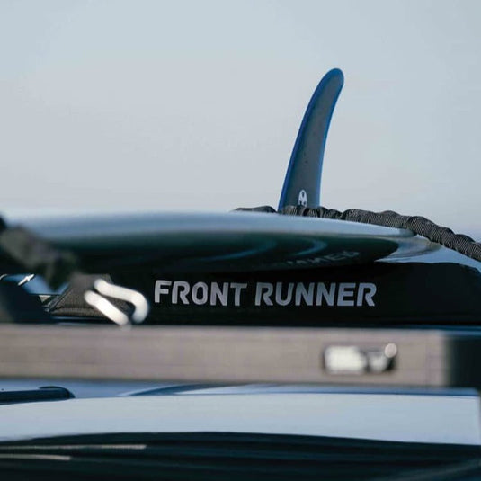 Close-up of Front Runner Rack Pad Set mounted on a vehicle roof rack with a surfboard fin visible in the background