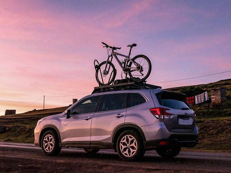 Load image into Gallery viewer, Front Runner Pro Bike Carrier mounted on a car roof at dusk with a scenic sunset background.
