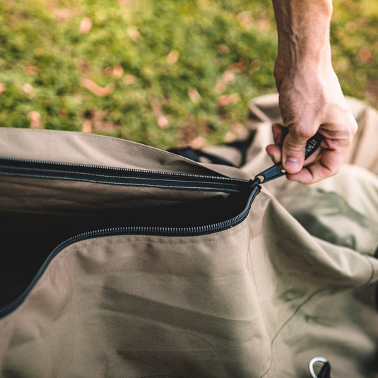 Person opening a water-resistant Gazelle Tents T3 Tandem duffle bag on grassy background.