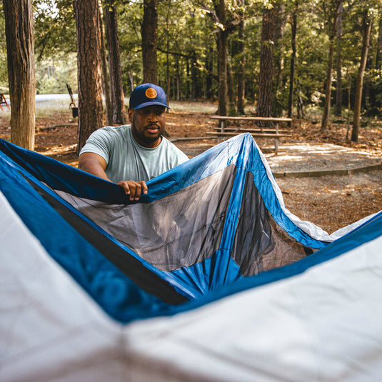 Man setting up a blue and gray Territory Tents Jet Set 3 Hub Tent in a campground