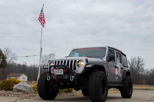 Jeep Wrangler outfitted with Fishbone Offroad Barracuda Modular Bumper, parked outdoor with American flag in background.