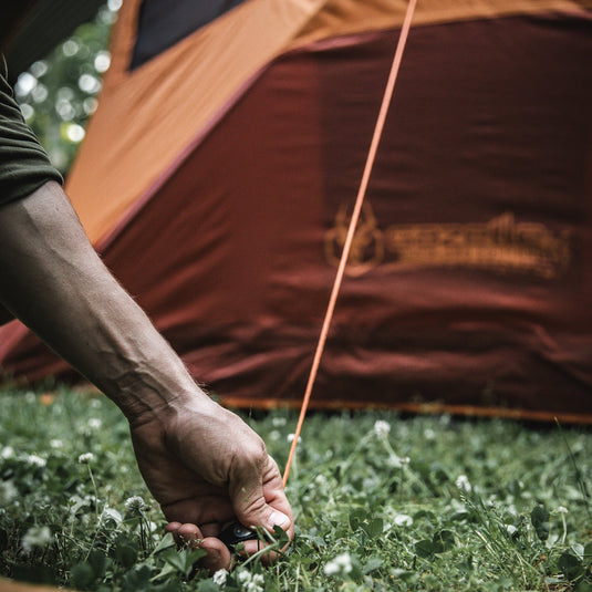 Person securing a tent with Gazelle Tents 12-Pack All-Terrain Stake in grassy campsite.