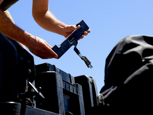 "Installation of Front Runner Wolf Pack Pro MKII Rack Mounting Bracket by person on vehicle storage box"