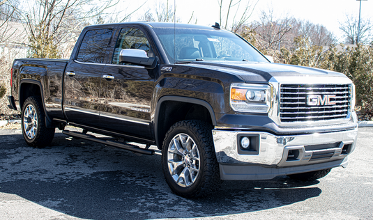 Alt text: "GMC Sierra crew cab with Fishbone Offroad 5 inch oval side steps installed, suitable for 2007-2019 Chevy/GMC 1500, 2500, 3500 models, shown parked outdoors."