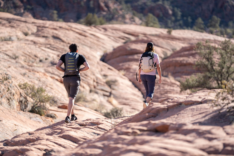 Load image into Gallery viewer, Two hikers with Klymit Echo 12L Hydration Packs trekking on rocky desert terrain.
