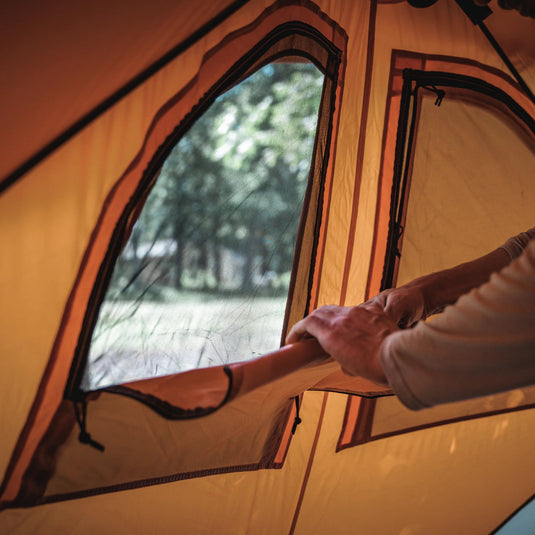 Person unzipping the window of a Gazelle Tents T8 Hub Tent from inside, with trees in the background.