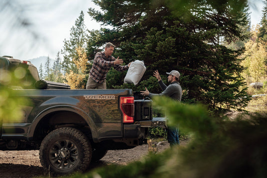 Two men exchanging Klymit Horizon Overland Blanket near truck during camping trip in the woods