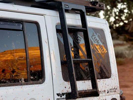 Alt text: "Front Runner Jeep Wrangler JK Side Mount Ladder attached to a white Jeep, covered in mud, showing rugged off-road use."