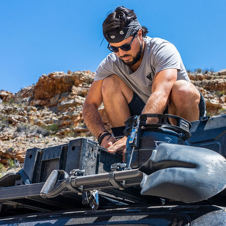 Load image into Gallery viewer, Man securing a spade to a Front Runner Ratcheting Spade/Shovel Mount on an off-road vehicle
