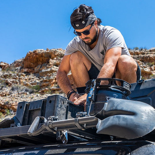 Man securing a spade to a Front Runner Ratcheting Spade/Shovel Mount on an off-road vehicle