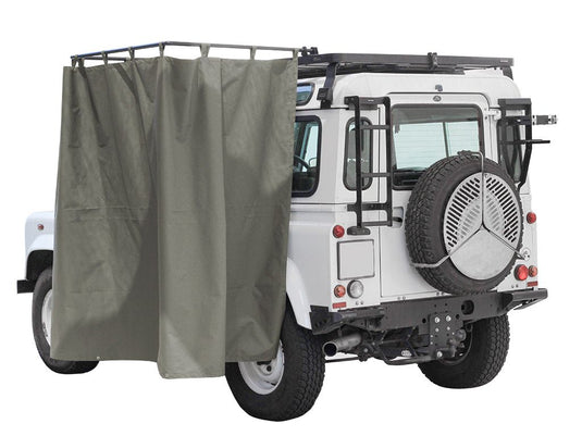 Rear view of a white off-road vehicle equipped with a Front Runner rack mounted shower cubicle with grey privacy curtains.