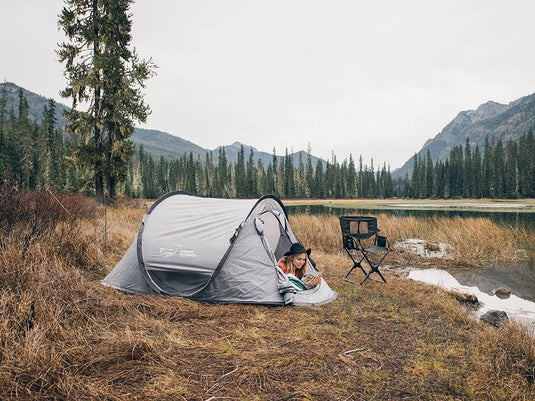 "Front Runner Flip Pop Tent set up in a scenic mountain location with a person sitting inside reading a book"