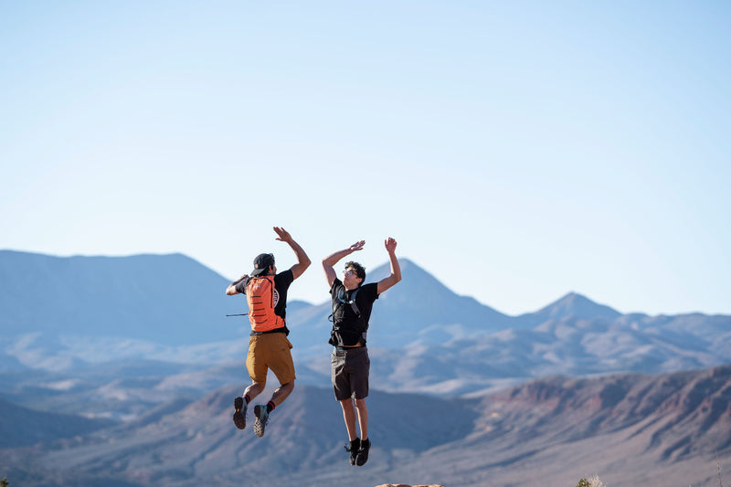 Load image into Gallery viewer, Two hikers celebrating with a jump in the mountains wearing Klymit Echo 12L Hydration Packs
