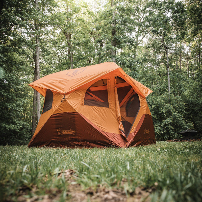 Load image into Gallery viewer, Gazelle Tents T4 Hub Tent Overland Edition set up in a forest clearing, showcasing its spacious design and orange exterior with company logo on display.
