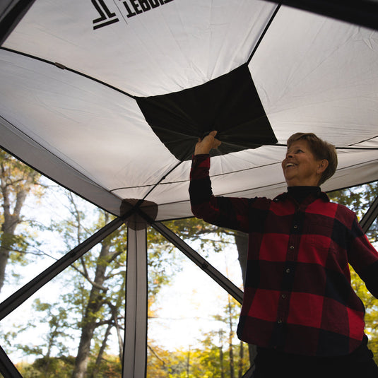 Person in a red and black checked shirt setting up a Territory Tents 4-Sided Portable Screen Tent outdoors.